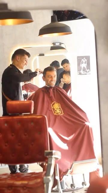Barbero cortando el cabello a un cliente con capa